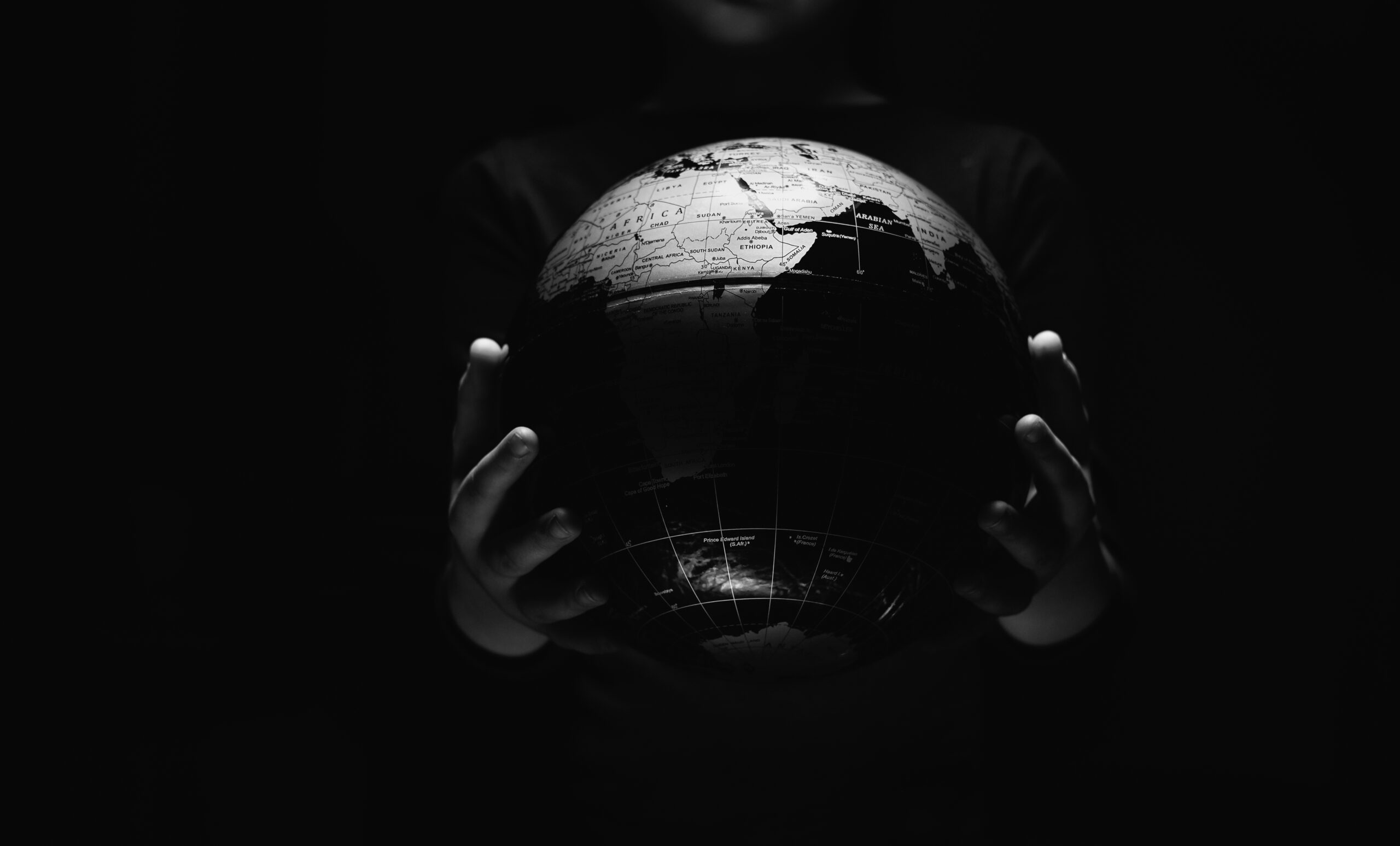 Hands of little girl hold globe sphere map isolated on black background.  COVID-19 pandemic infection disease. Environmental pollution, ecological disaster our kids and future planet concept BW image
